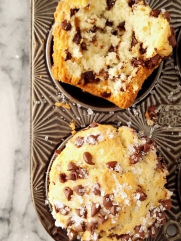 Whole and halved bakery-style chocolate chip muffins in a tin