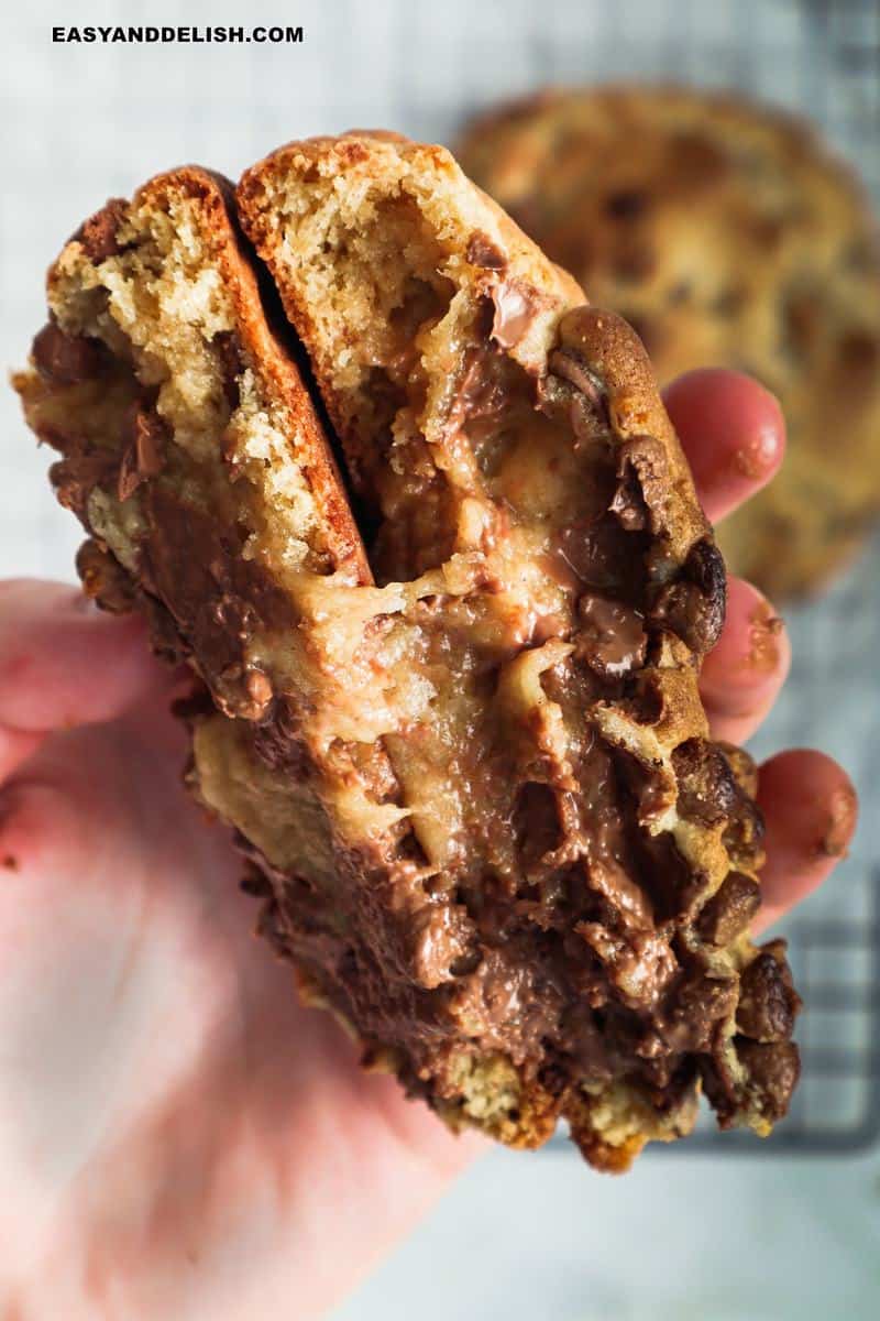 a hand holding 2 halves of levain cookies with gooey middle