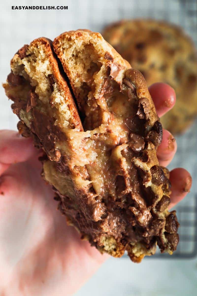 A hand holding 2 halves of levain cookies with gooey middle.