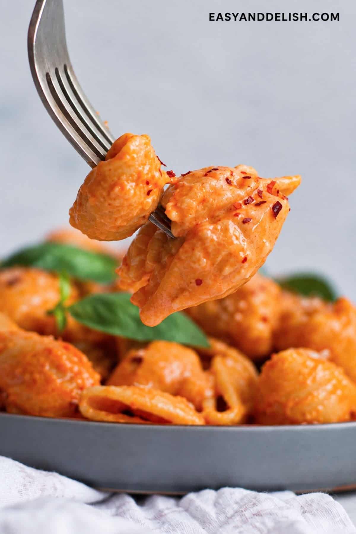 Creamy shell pasta with red pepper flakes lifted on a fork.