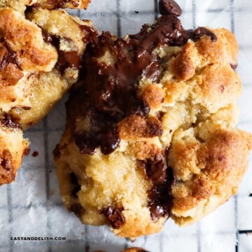 close up of a chocolate chip walnut cookie cut in half and showing puddles of melty chocolate