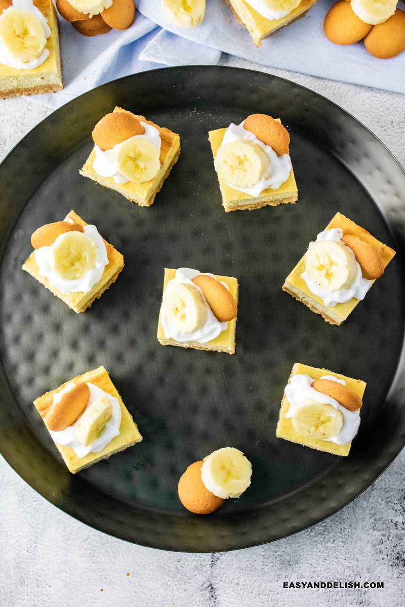 a tray full of banana pudding cheesecake squares topped with whipped cream, wafers, and banana slices