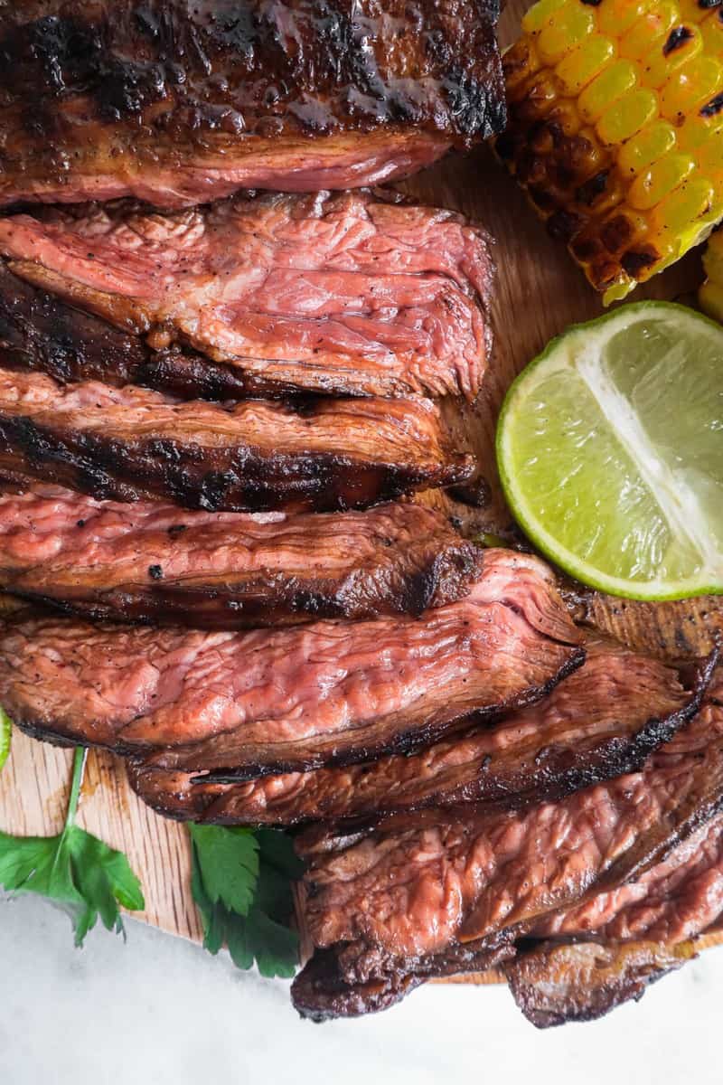 sliced marinated grilled flank steak with garnishes on the side