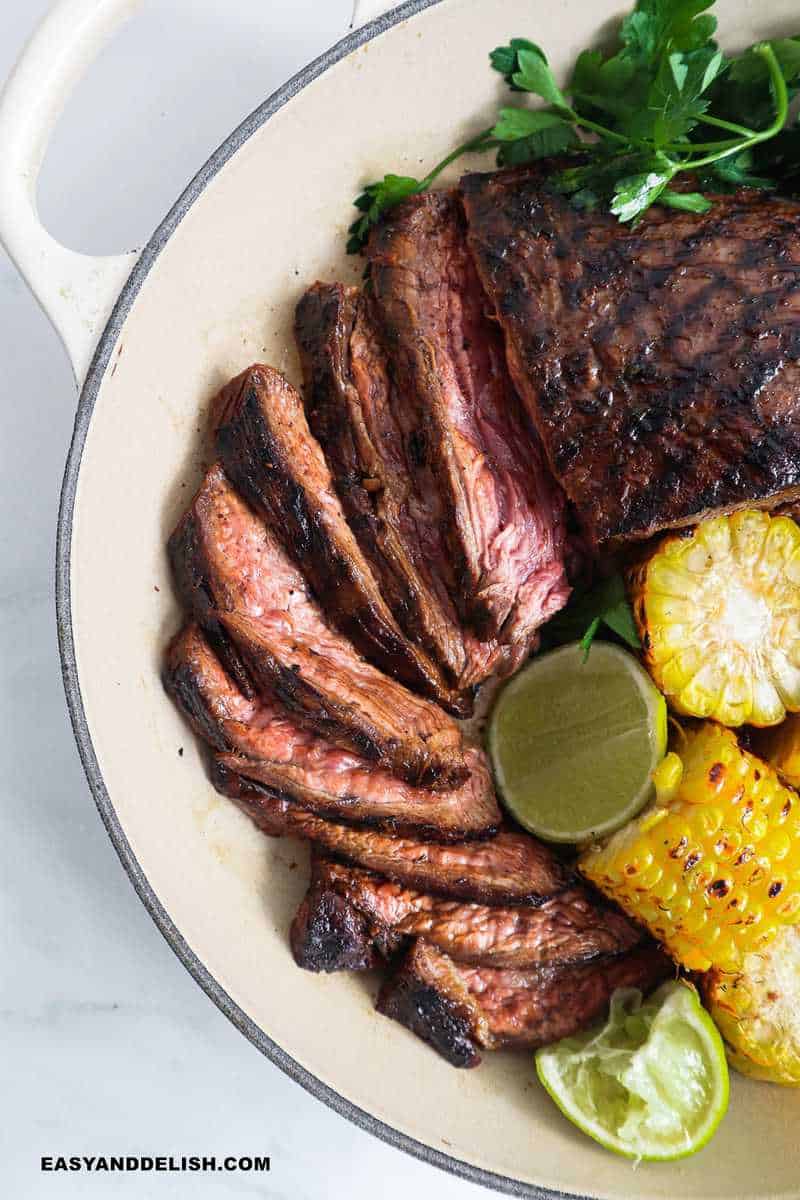 sliced meat in a skillet with veggies and lime wedges