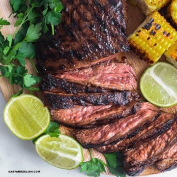 close up of grilled flank steak, sliced with a side of lime wedges and grilled corn