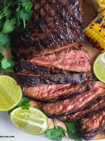 close up of grilled flank steak, sliced with a side of lime wedges and grilled corn