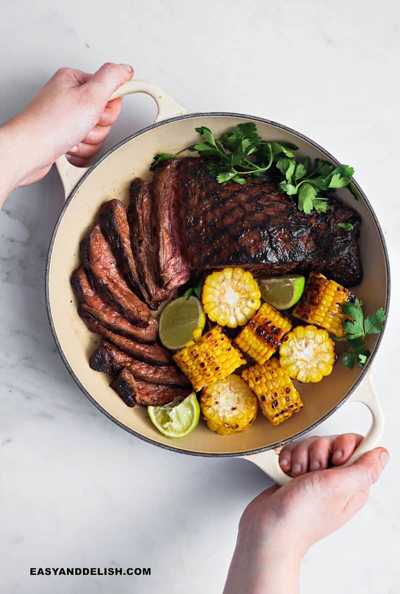 sliced flank steak with garnishes in a skillet held with 2 hands as part of our easy steak dinner ideas