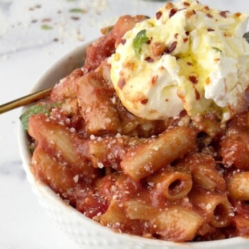 close up of a bowl of penne pomodoro with burrata on top