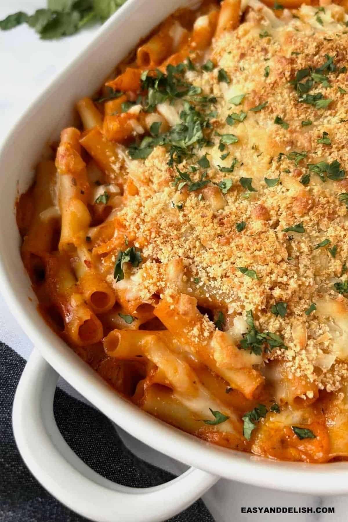 Baked ziti in a white casserole dish with browned panko, melted cheese, and chopped parsley on top.