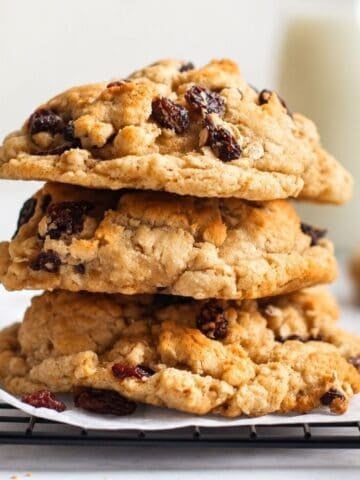 Thick oatmeal raisin cookies stacked on parchment paper over a cooling rack.