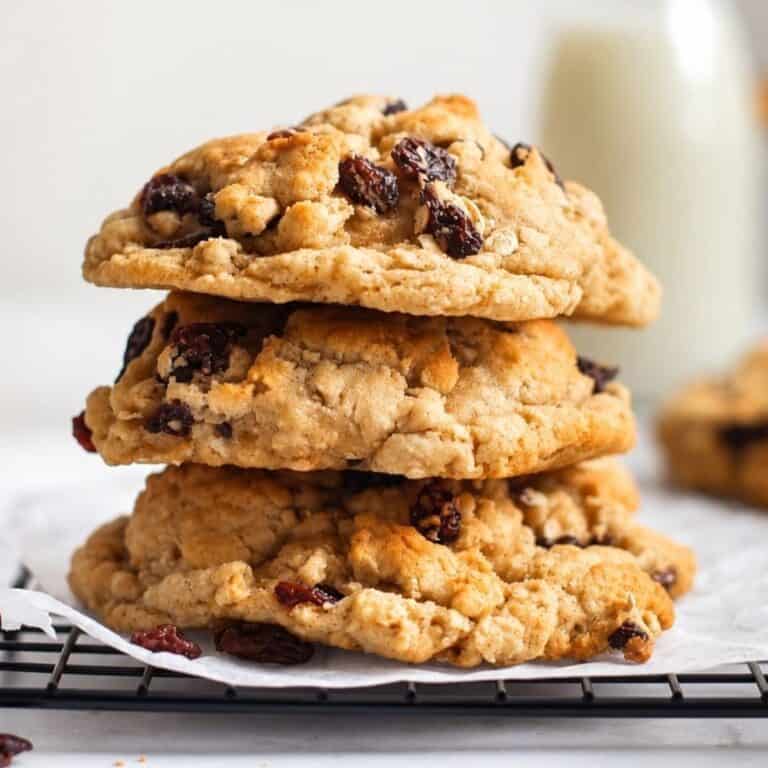 Thick oatmeal raisin cookies stacked on parchment paper over a cooling rack.