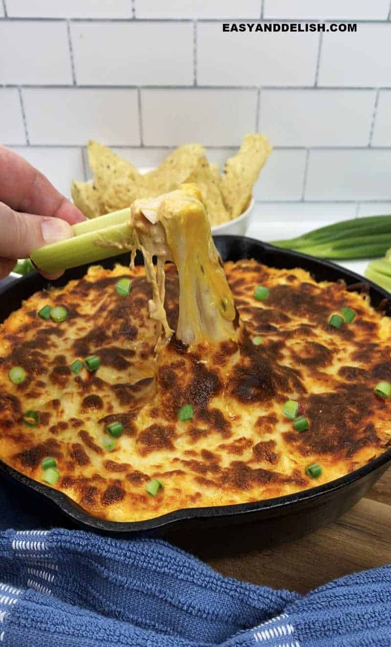 keto buffalo chicken dip skillet with a tortilla chips pulling the melted cheeses up