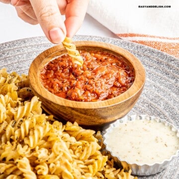 pasta chip dipped in spicy marinara sauce with more pasta chips on the side and another bowl of sauce
