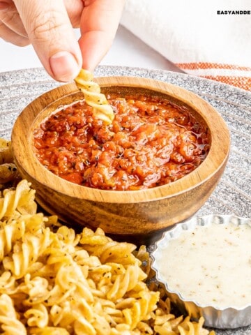 pasta chip dipped in spicy marinara sauce with more pasta chips on the side and another bowl of sauce