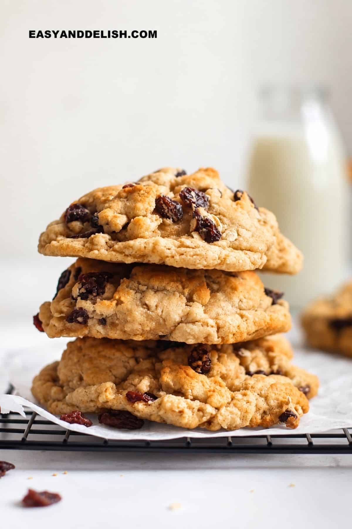 Thick raisin and oat cookies stacked on parchment paper over a wire cooling rack.