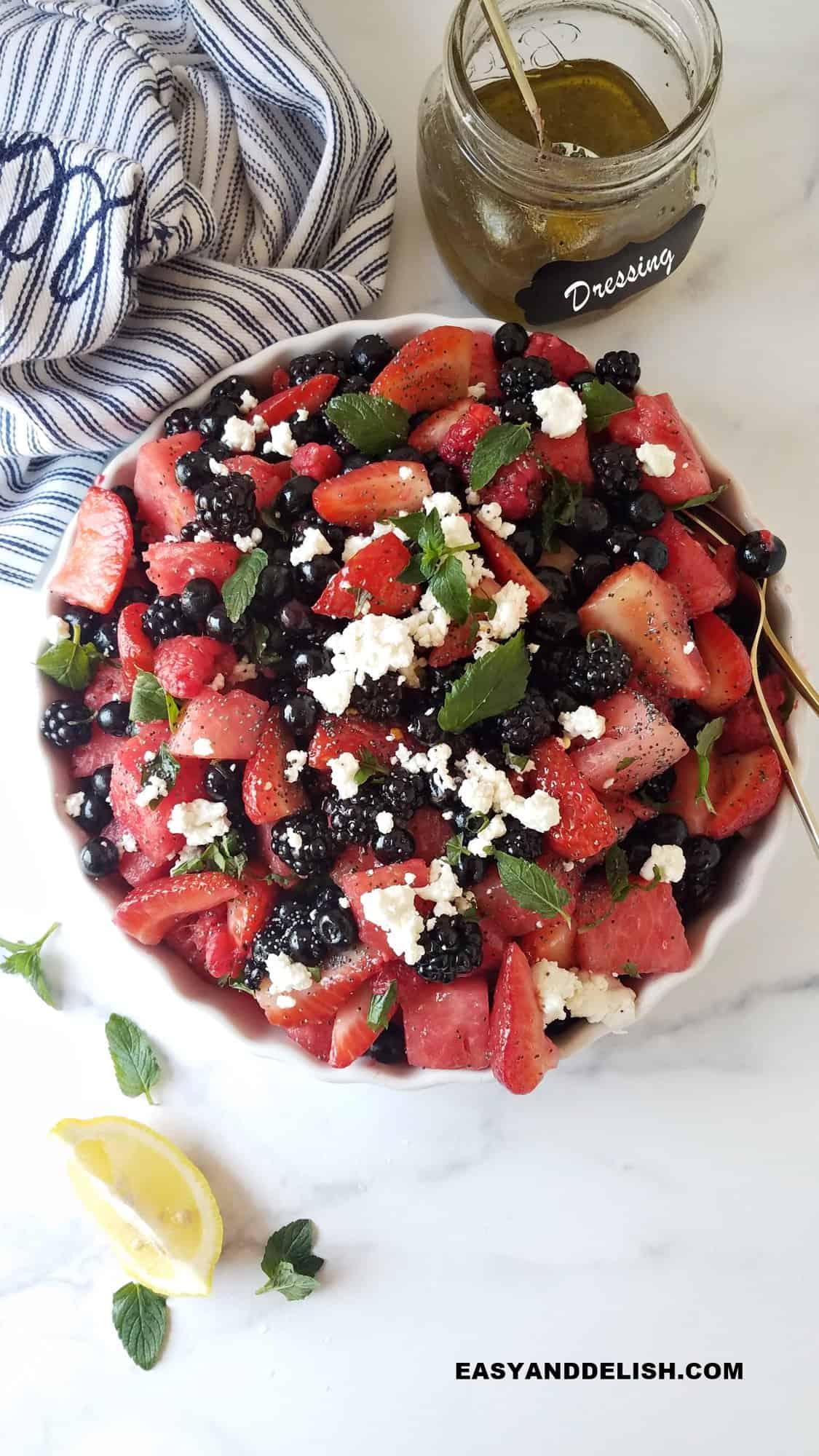 a large bowl of berry salad topped with goat cheese and mint 