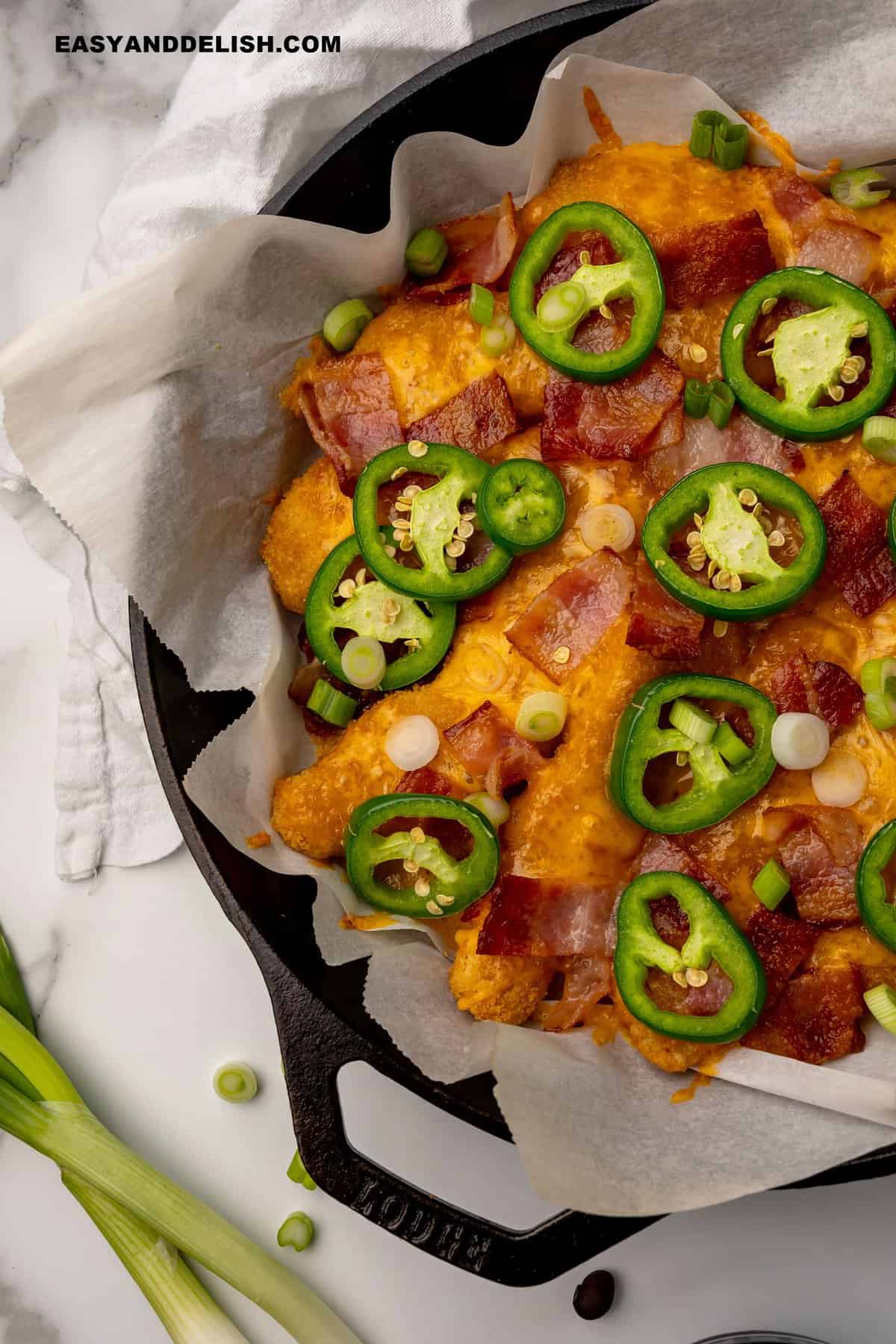 keto laoded chicken nachos in a cast-iron skillet with garnishes on the side