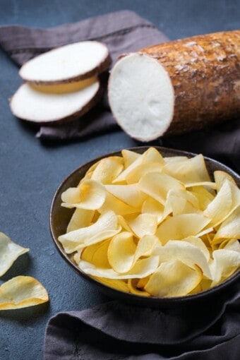 uma tigela com chips de mandioca e uma macaxeira ou aipim fatiado