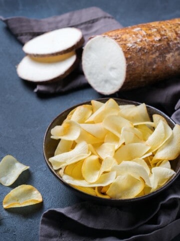 uma tigela com chips de mandioca e uma macaxeira ou aipim fatiado