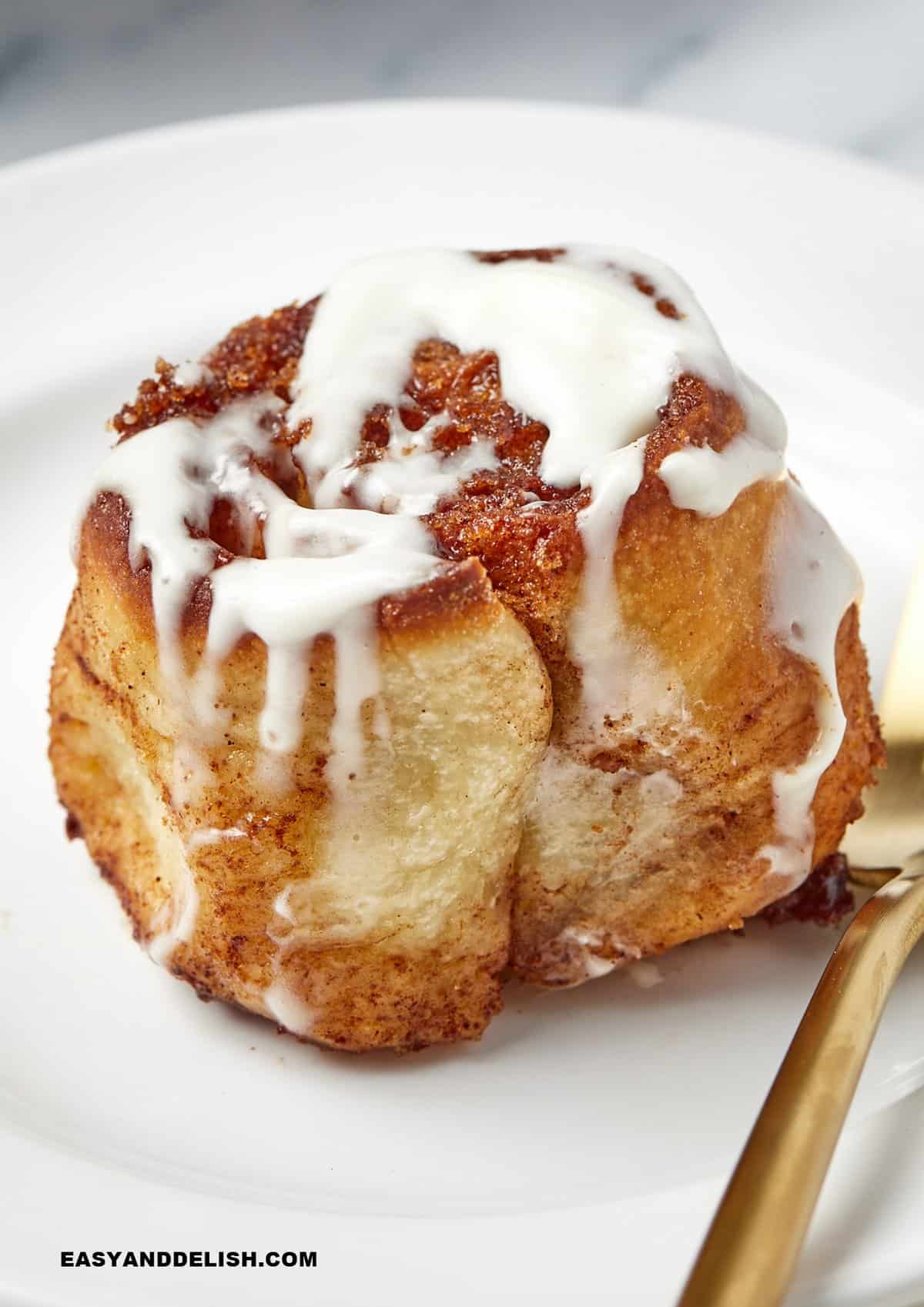 one baked good in a plate with icing on top and a fork on the side