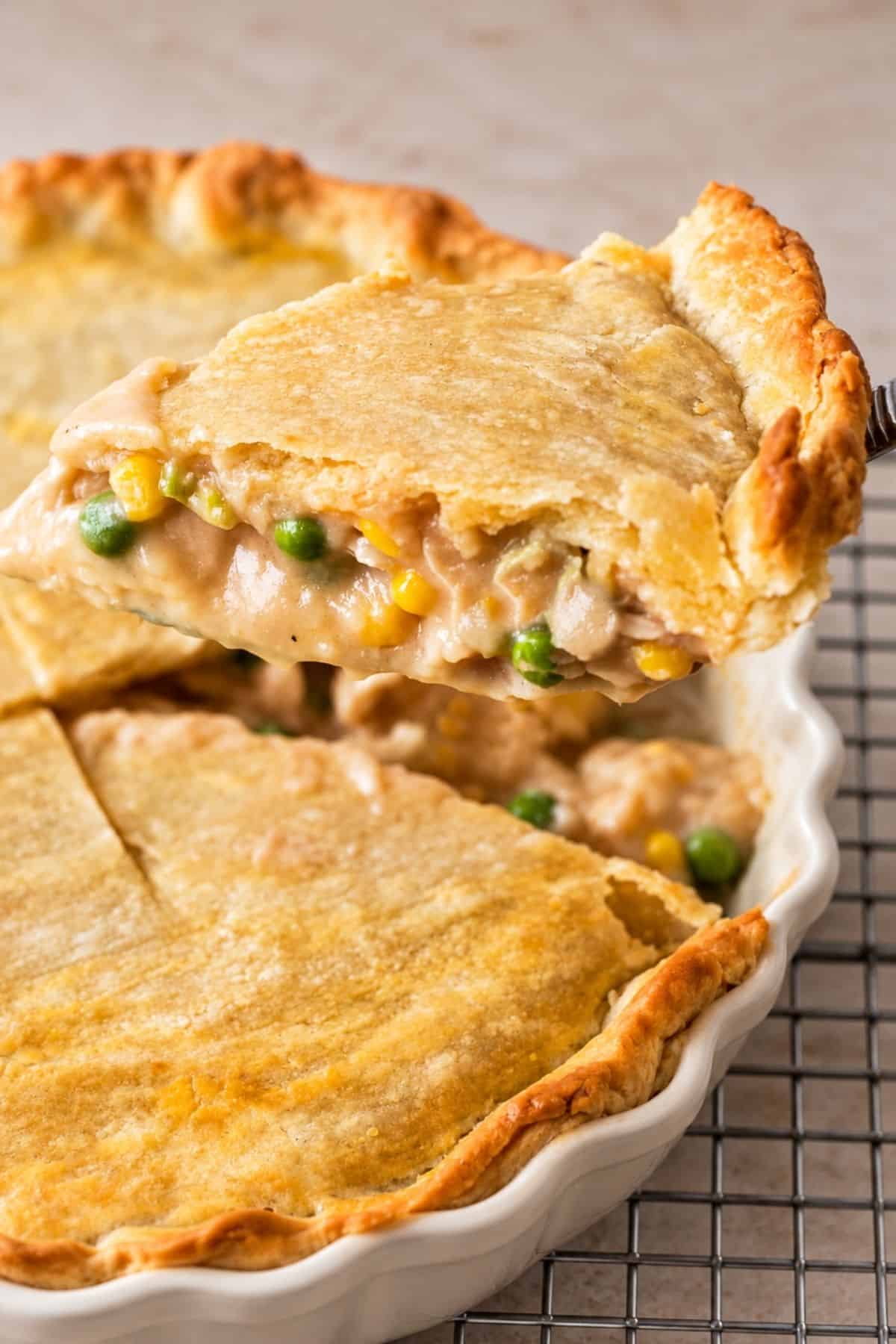A slice of Brazilian chicken pie lifted on a spatula, revealing creamy chicken, peas, and corn beneath the pastry crust.