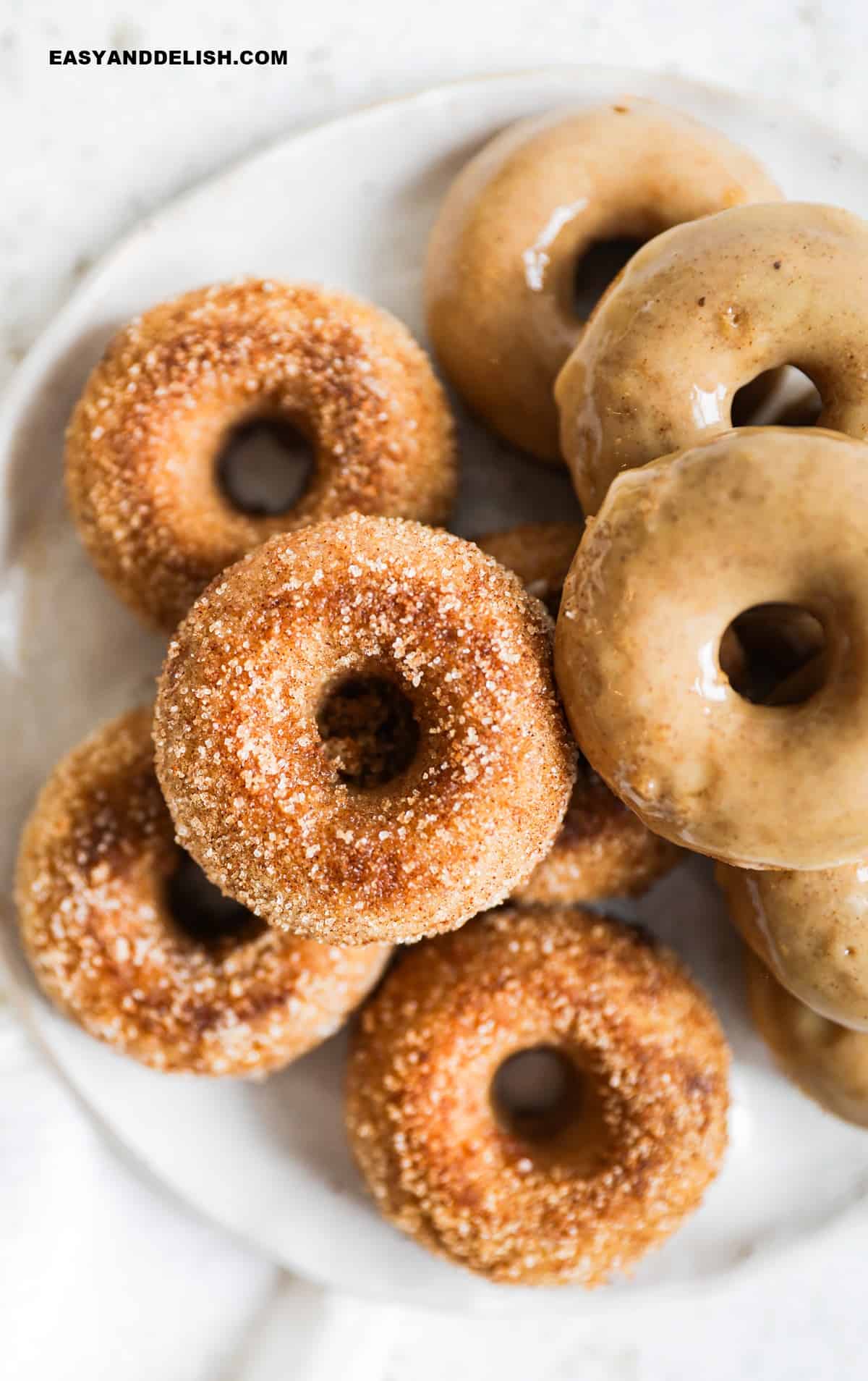 rosquinhas americanas com açúcar e canela e outras com glacê em um prato.