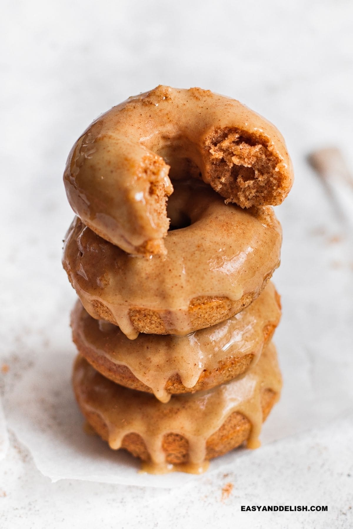 Maple-glazed cider donuts stacked on a plate with one donut showing the inside.