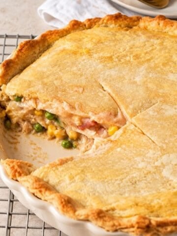 Brazilian chicken pot pie with a slice removed, revealing shredded chicken, peas, and corn beneath a golden crust in a ceramic dish.