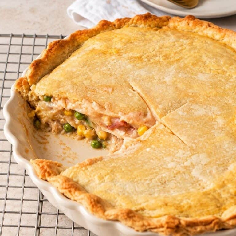 Brazilian chicken pot pie with a slice removed, revealing shredded chicken, peas, and corn beneath a golden crust in a ceramic dish.