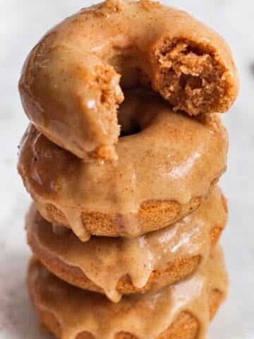 Baked apple cider donuts stacked with maple glaze and a bitten donut on top.