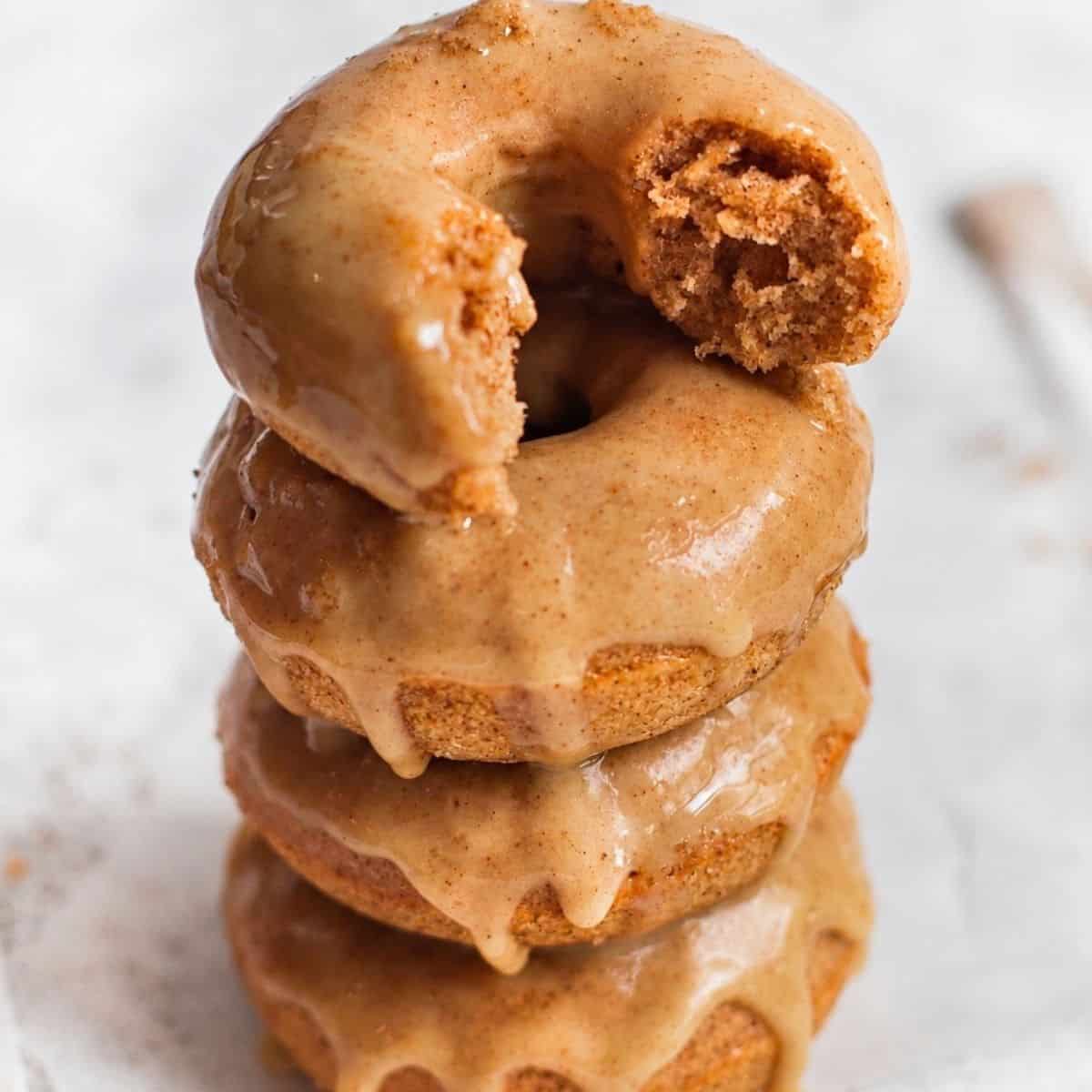 Baked apple cider donuts stacked with maple glaze and a bitten donut on top.