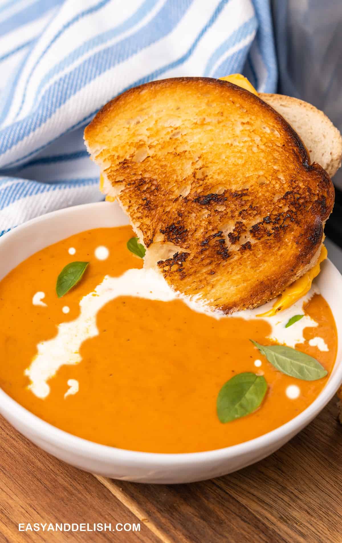 sandwich half dipped in abowl of creamy tomato soup