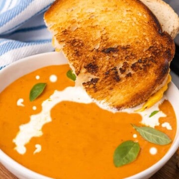 sandwich half dipped in abowl of creamy tomato soup