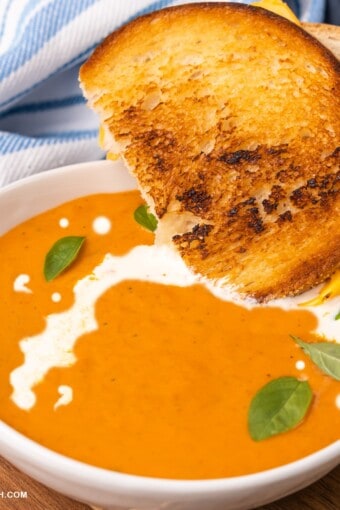 close up de uma tigela de sopa de tomate cremosa com um sanduiche