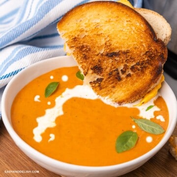 close up de uma tigela de sopa de tomate cremosa com um sanduiche