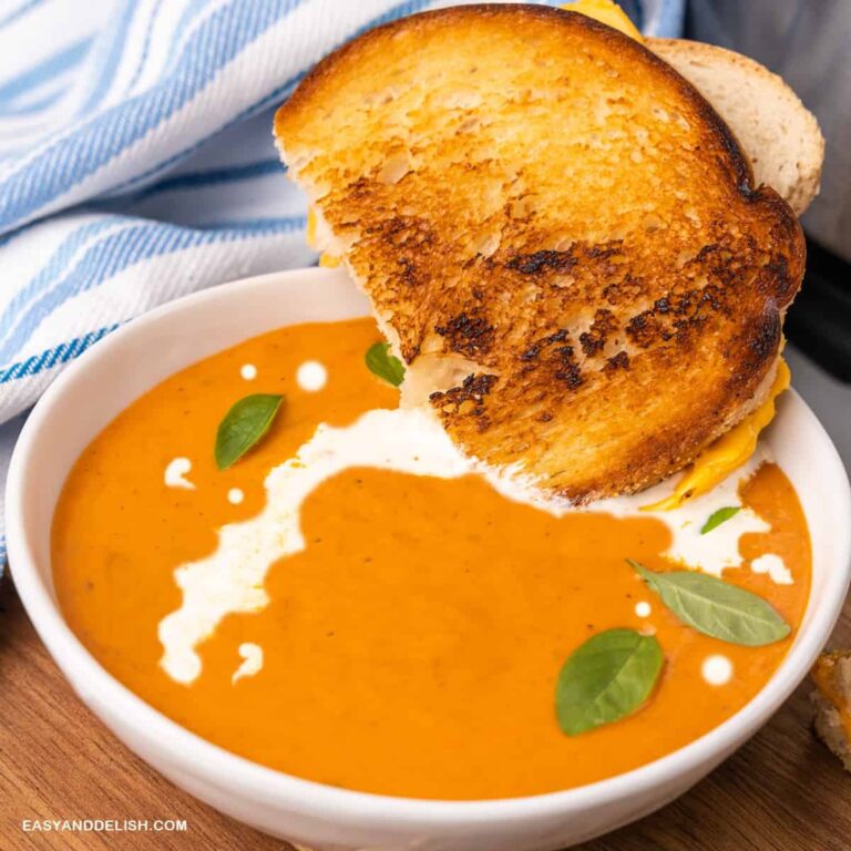 close up de uma tigela de sopa de tomate cremosa com um sanduiche