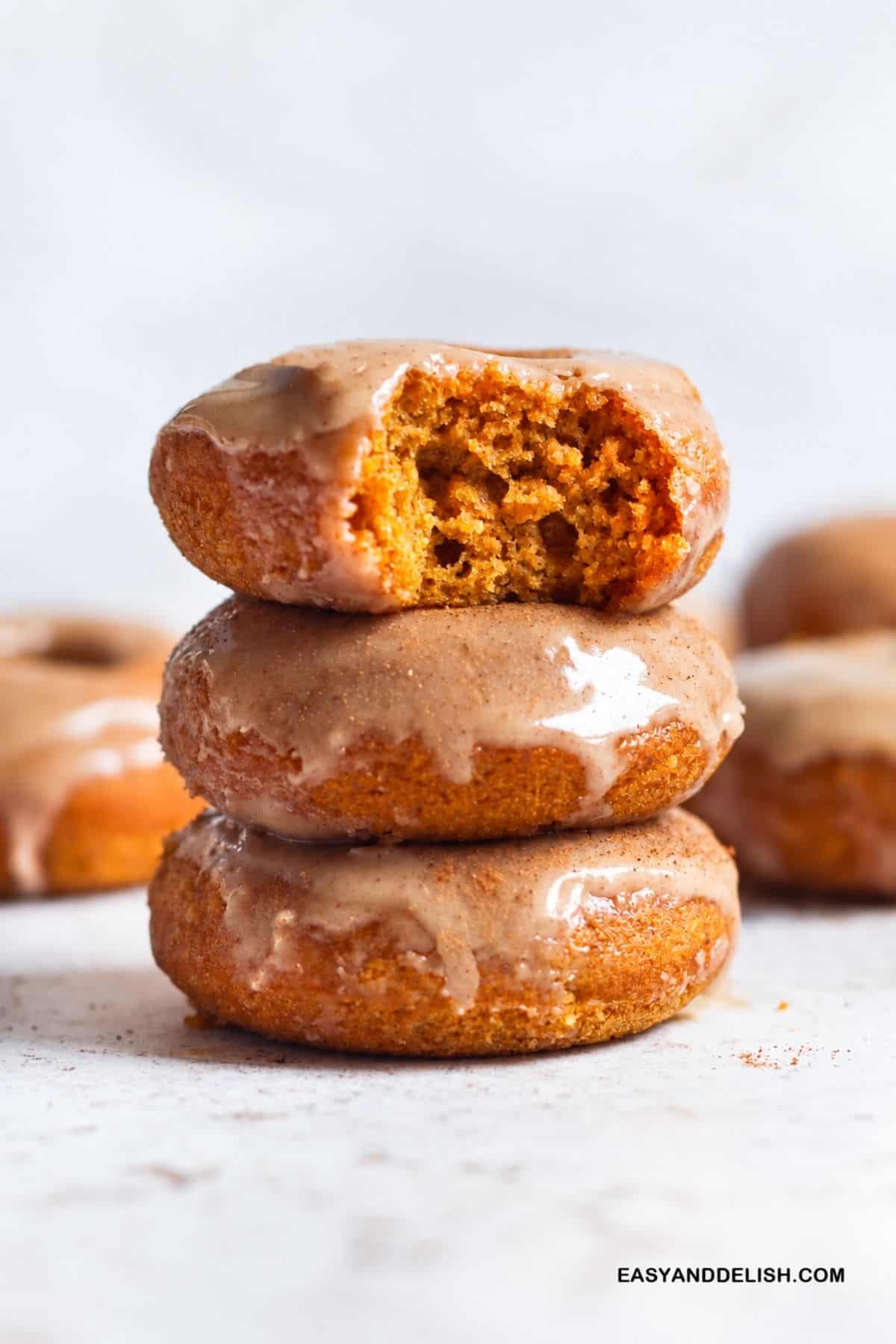 Stacked maple glazed donuts with one broken open to show the pumpkin crumb.