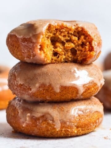 Three maple glazed donuts stacked with the top donut broken open to show its soft crumb.