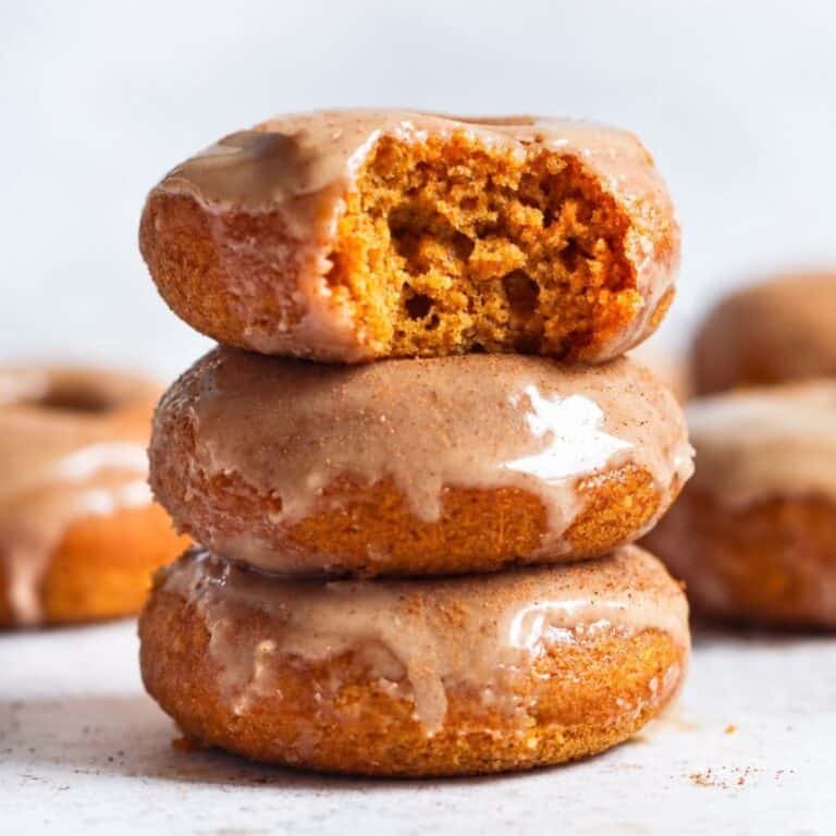 Three maple glazed donuts stacked with the top donut broken open to show its soft crumb.