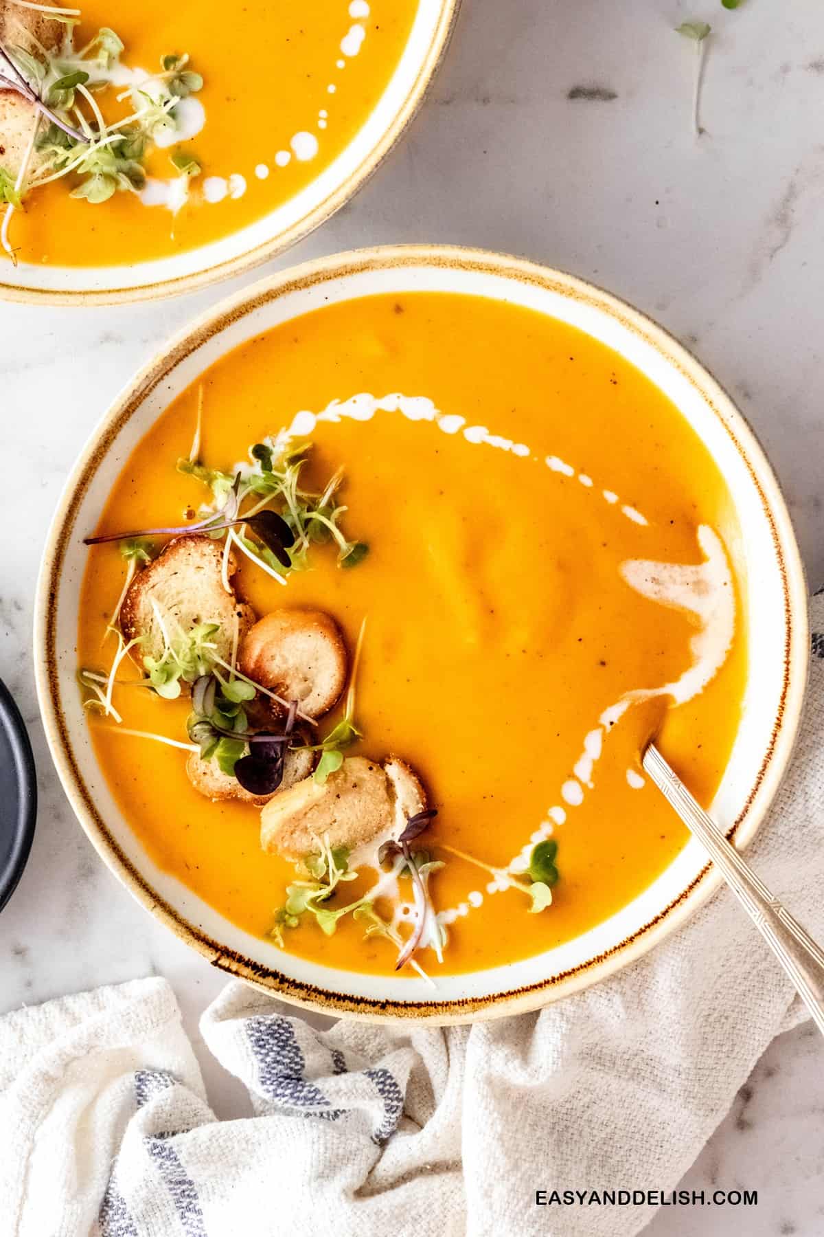 two bowls of creamy sweet potato soup garnished with herbs and croutons