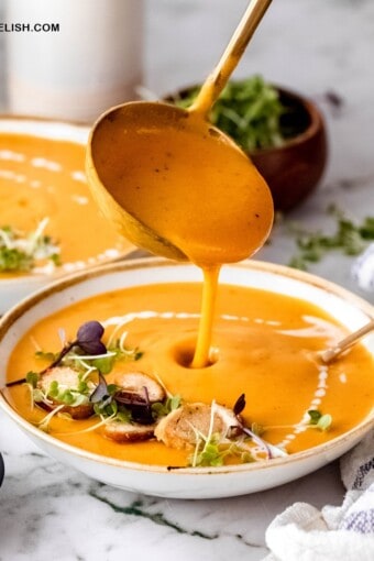 close up of a ladle filling a bowl of creamy sweet potato soup with carrots and coconut milk