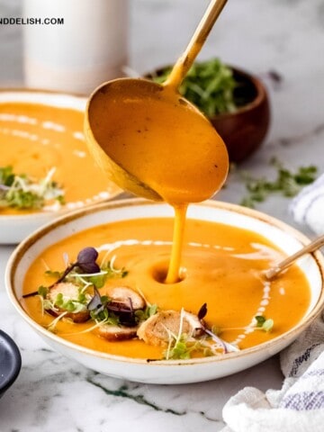 close up of a ladle filling a bowl of creamy sweet potato soup with carrots and coconut milk