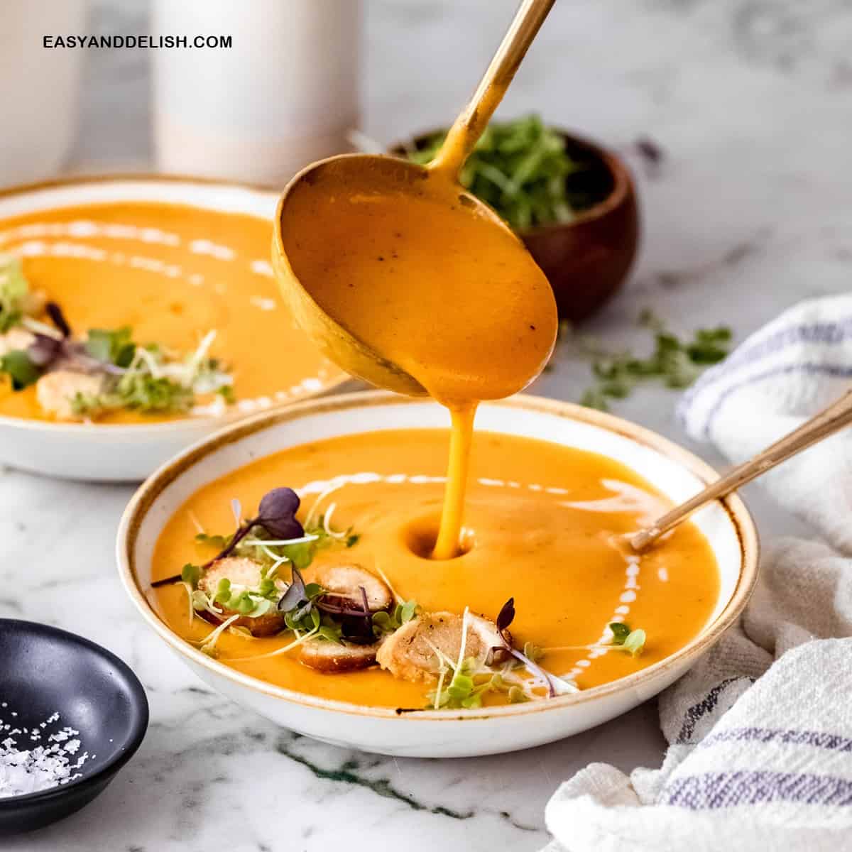 close up of a ladle filling a bowl of creamy sweet potato soup with carrots and coconut milk