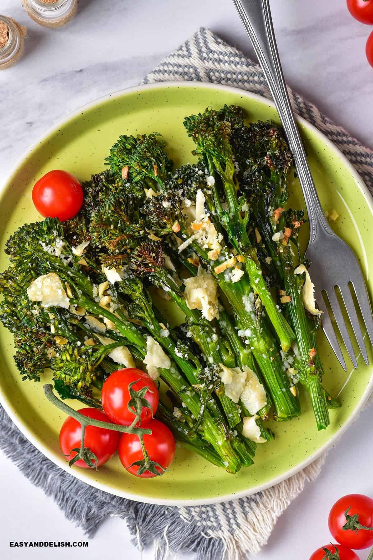 air fryer broccolini in a plate with cherry tomatoes on the vine on the side