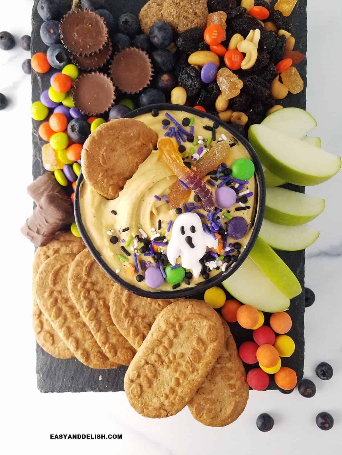 a board with apple slices adn cookies witha  bowl of pumpkin dip in the center