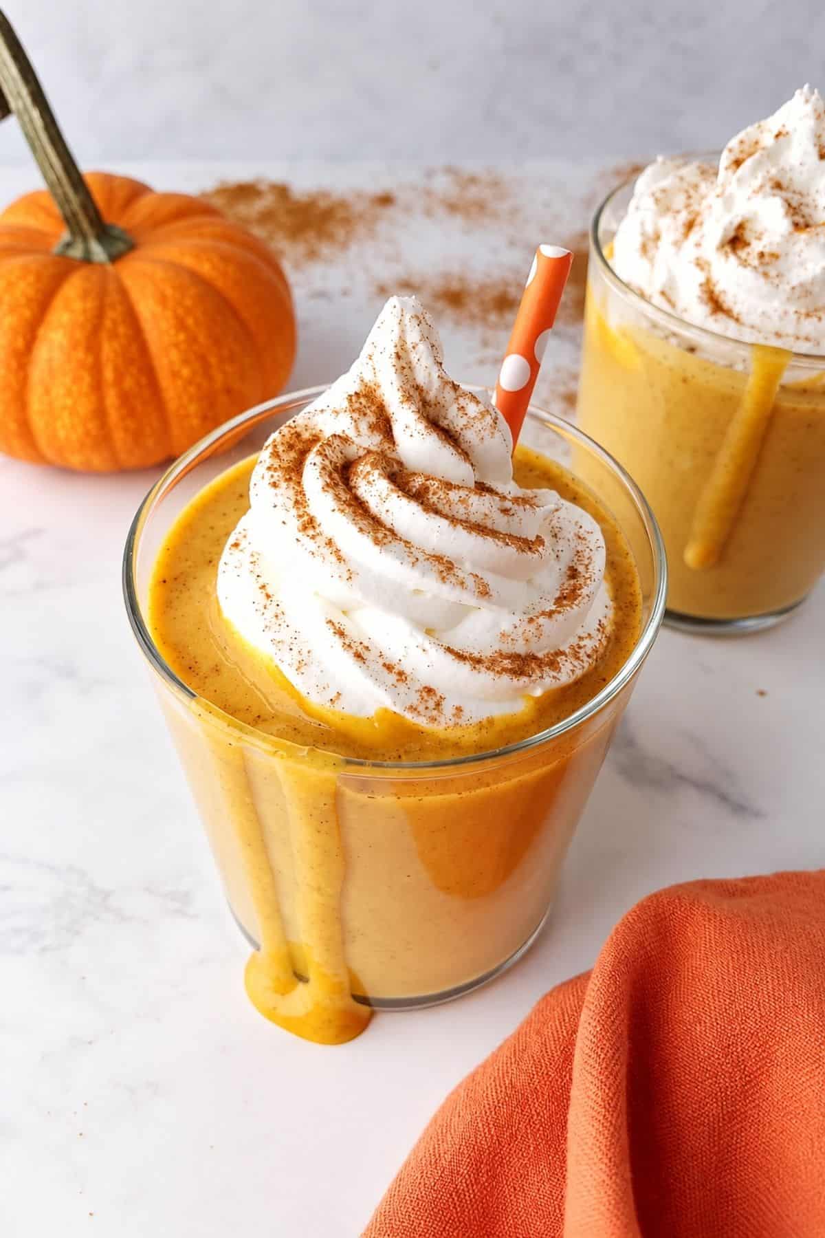 Close-up of a creamy pumpkin shake with whipped topping, spice, and an orange straw.
