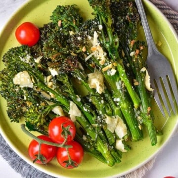 air fryer broccolini in a plate with cherry tomatoes on the vine on the side