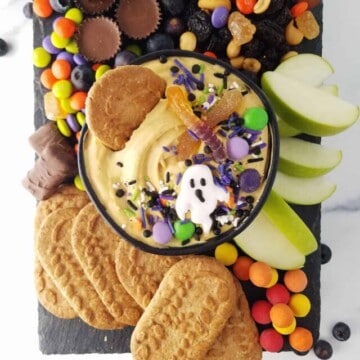 a board with apple slices adn cookies witha bowl of pumpkin dip in the center