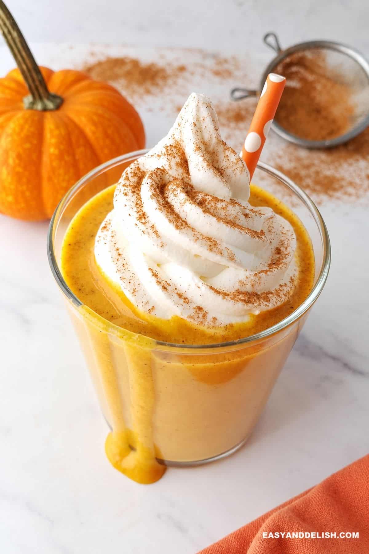 Pumpkin spice protein shake topped with whipped cream and spice beside a second glass and small pumpkin.