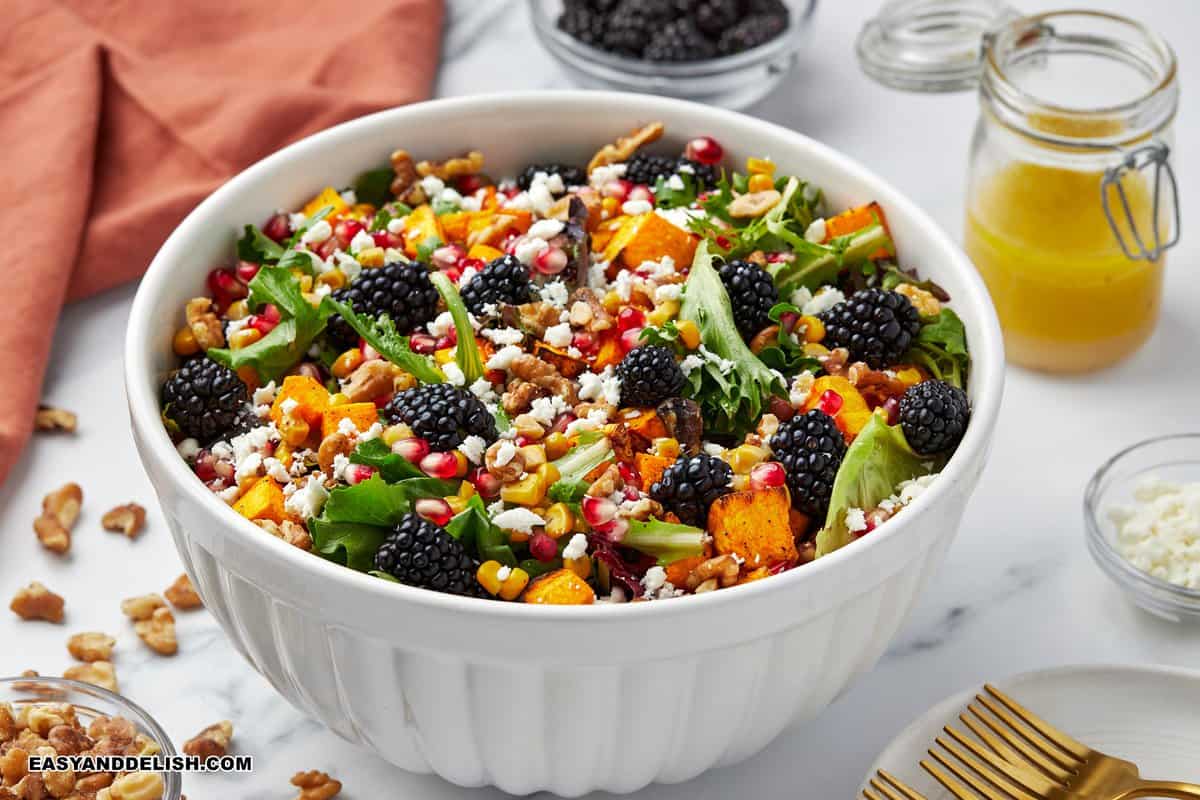 A bowl of butternut squash salad with garnishes on the side.